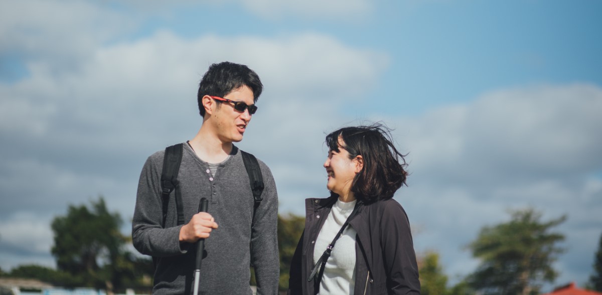 杖を持つ男性と隣で歩く女性が笑顔で向き合う